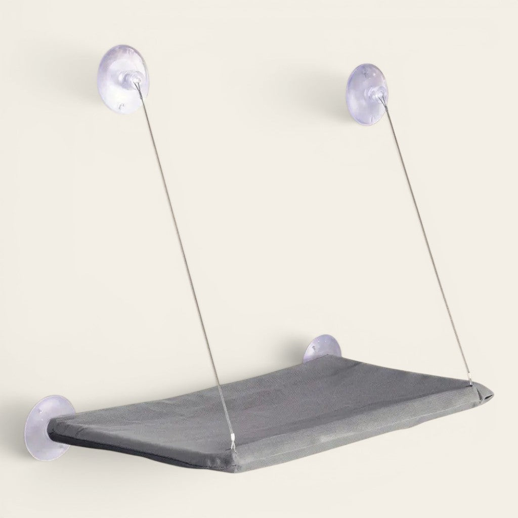 Hamac ventouse chat gris fixé à la fenêtre avec ventouses renforcées pour offrir un espace de repos en hauteur.
